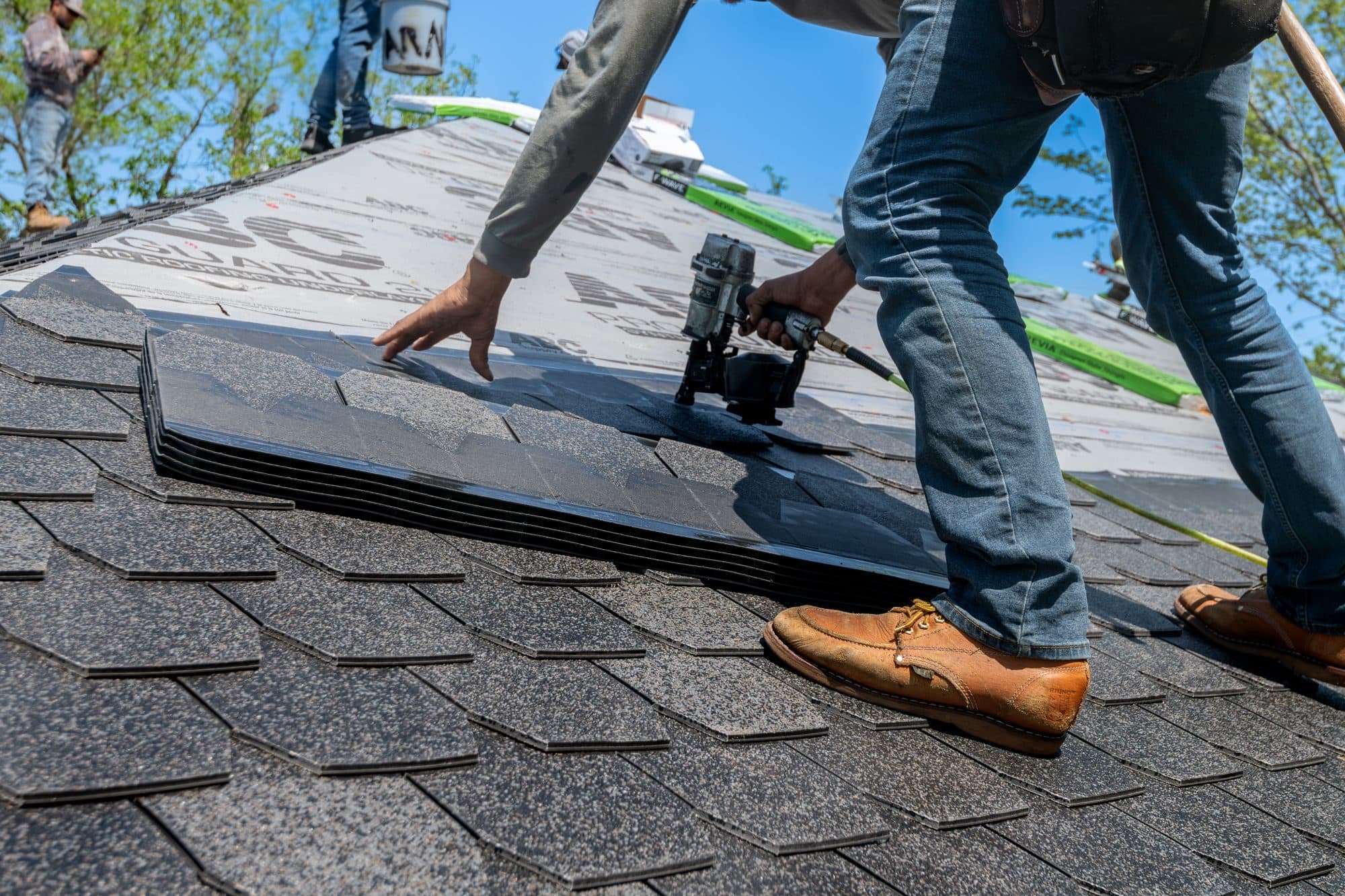 Roofer nailing asphalt shingles on a sloped roof
