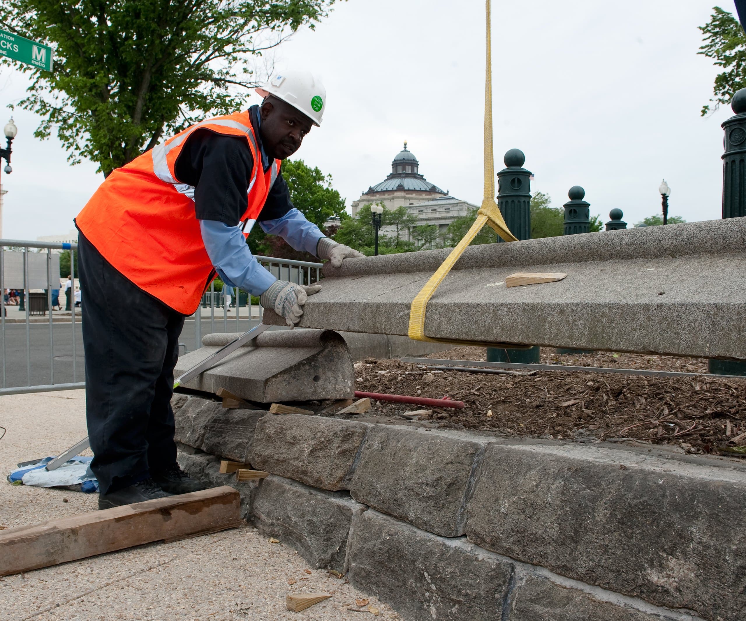 Mason setting a granite coping stone on a cut-stone wall